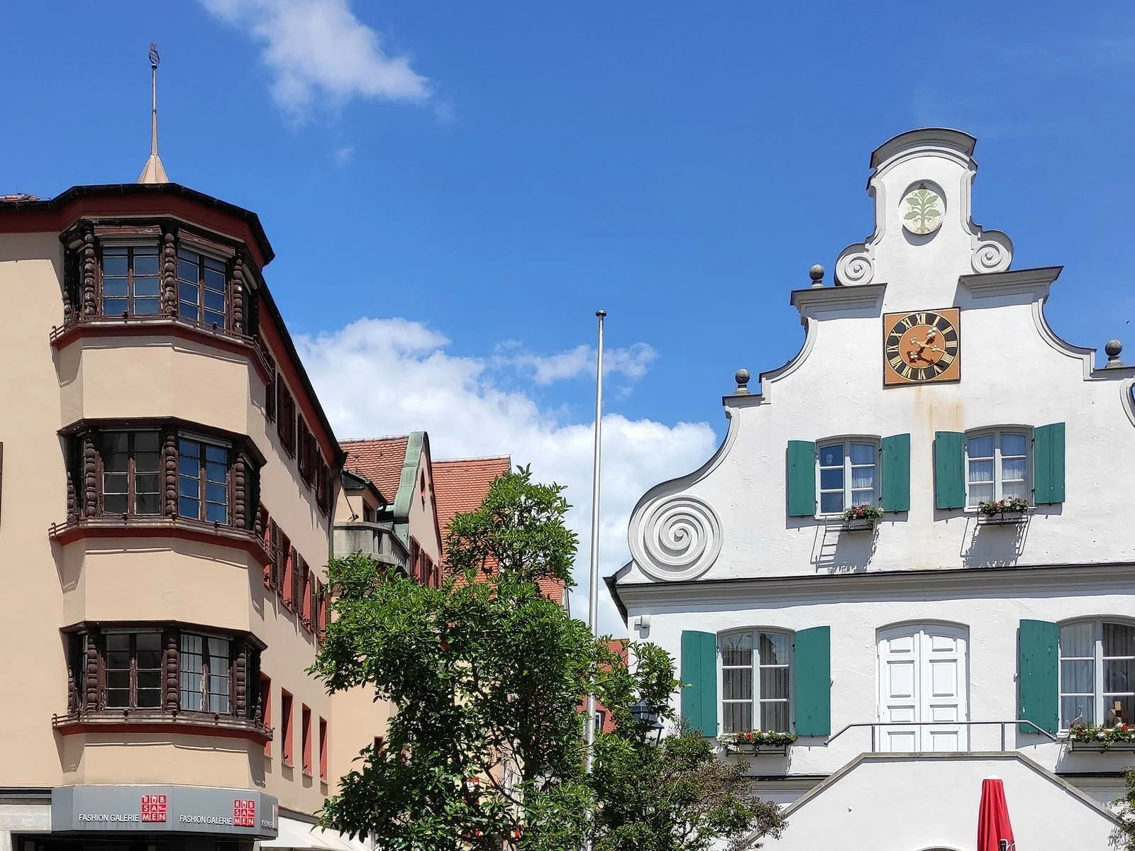 Das barocke Rathaus von Aichach mit Turmuhr und geschweiftem Giebel, daneben ein Bürgerhaus mit Erkerfenstern
